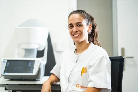Cristina Berbés, especialista de Oftalmediq, sentada en la sala de pruebas diagnósticas junto a un campímetro computarizado.
