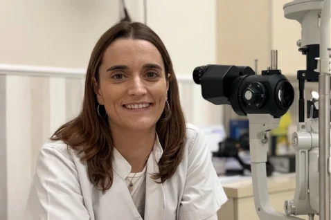 La Dra. Marta Carrera Tarrés posando en su consulta de Oftalmediq junto a una lámpara de hendidura para exámenes oculares.
