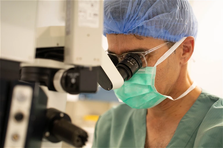 Cirujano oftalmológico realizando procedimiento de precisión en quirófano, equipado con microscopio quirúrgico para intervenciones de blefaroplastia y oculoplastia.