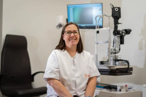 Laia Pascual Batlle, especialista en salud ocular, en un entorno clínico equipado con pantallas de análisis visual y retinógrafo.
