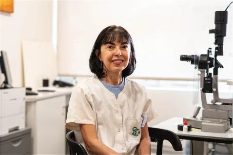 Mercedes Vázquez Barrero, profesional de Oftalmediq, sentada en su despacho frente a equipos de tecnología óptica.